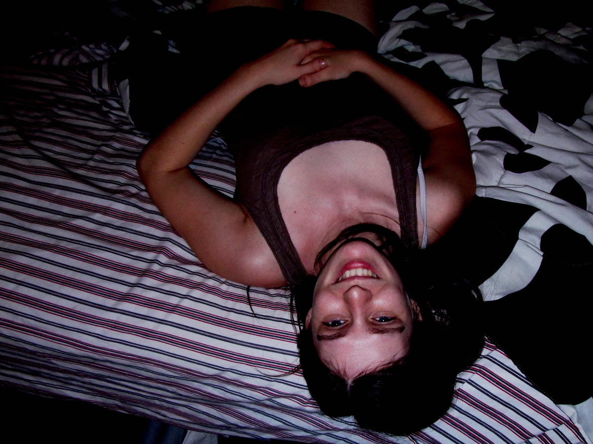 A beautiful feminine person with dark hair upside down on a bed