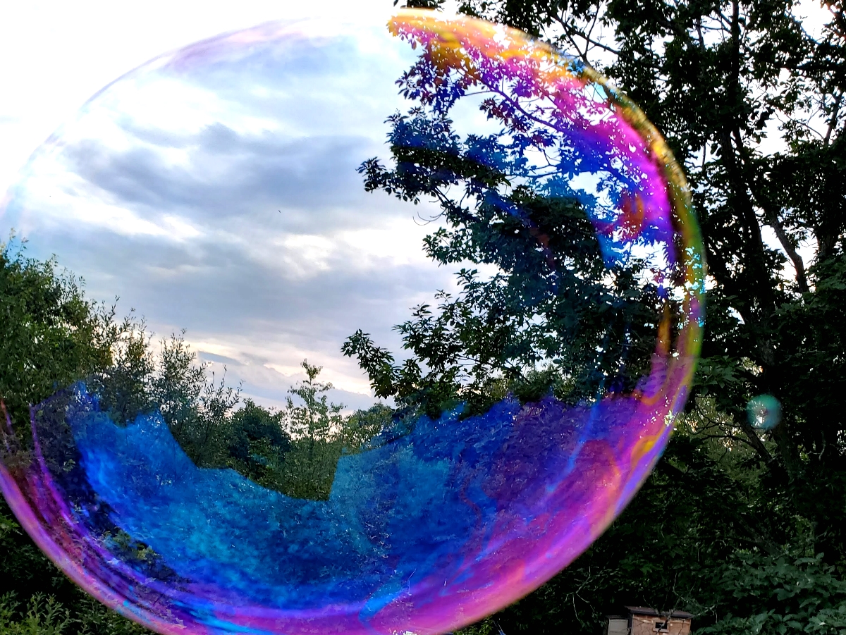 A large, colorful bubble in front of trees and the sky