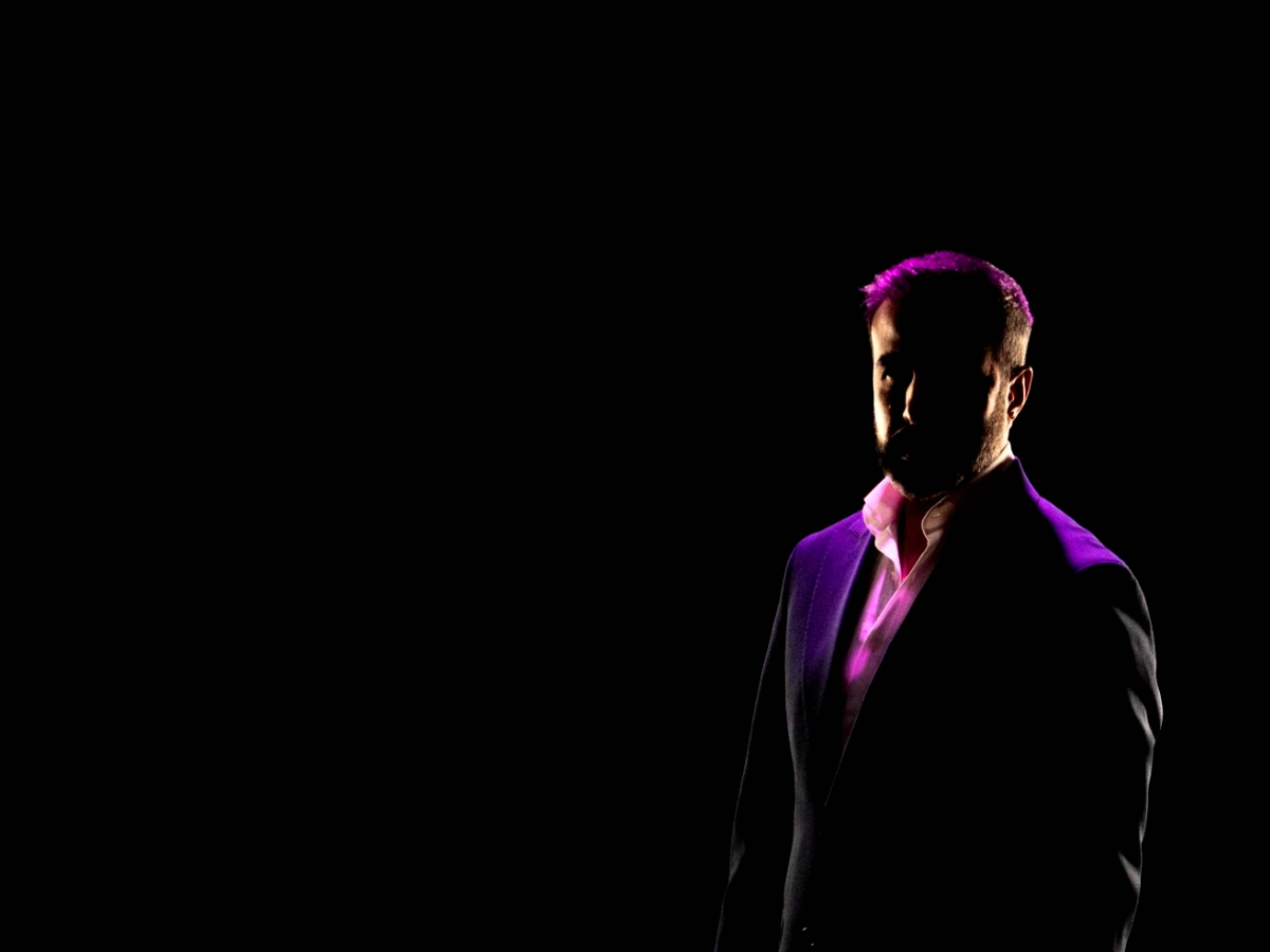 A man in a black suit, standing in the darkness