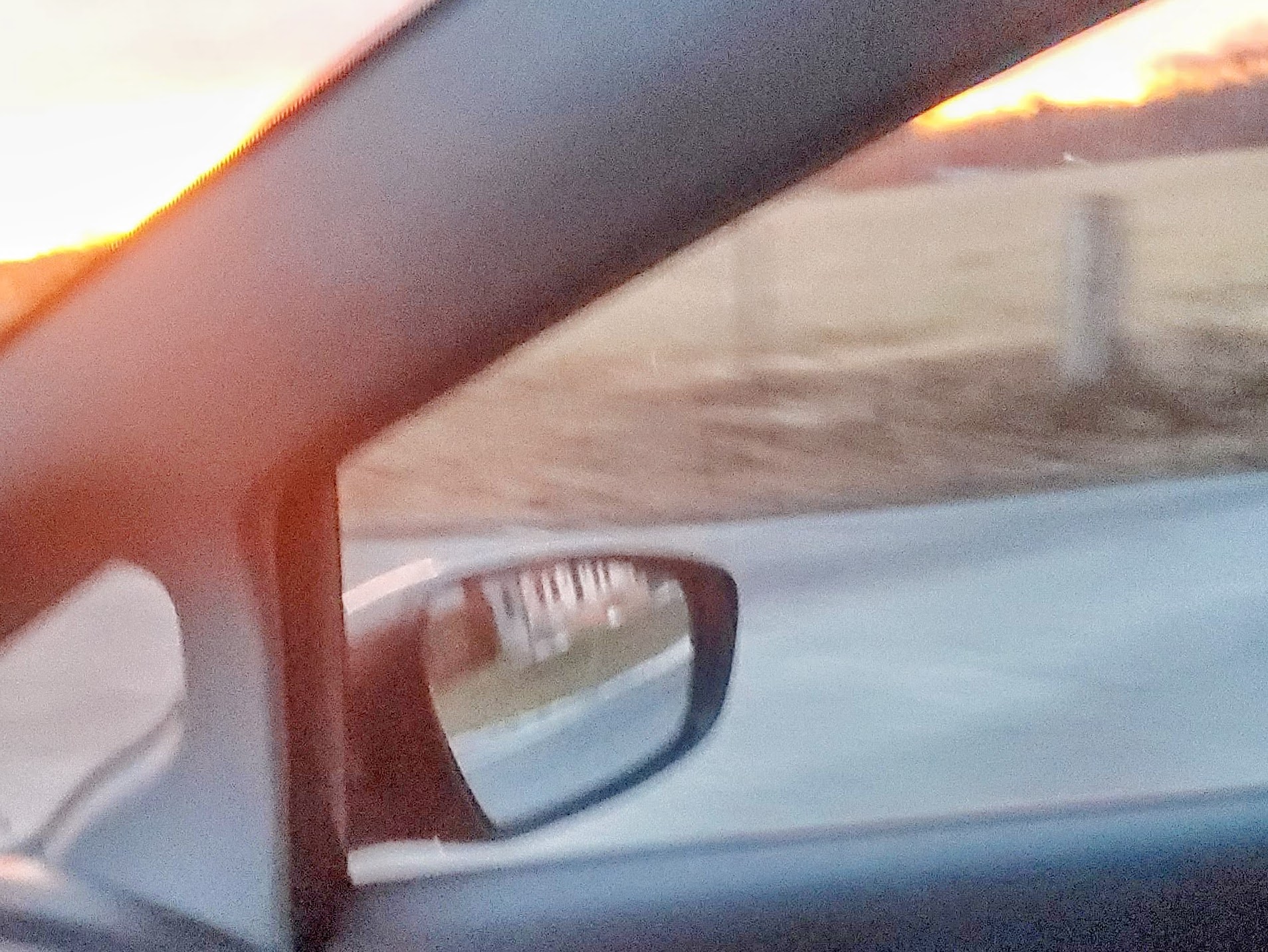A sunset through a passenger's side door on the road