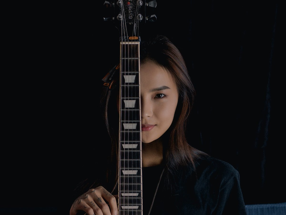 An attractive Asian woman, her face half-covered by a guitar